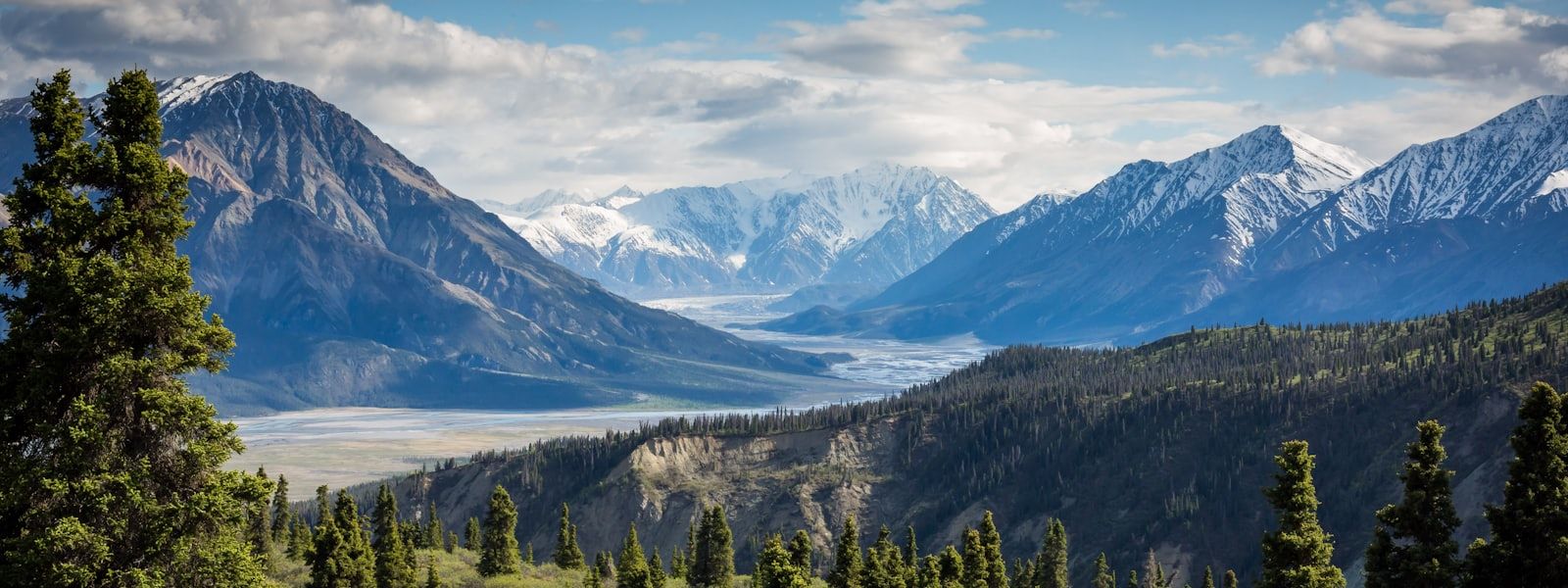 A wide mountain range with snow-capped peaks above a green valley at first light